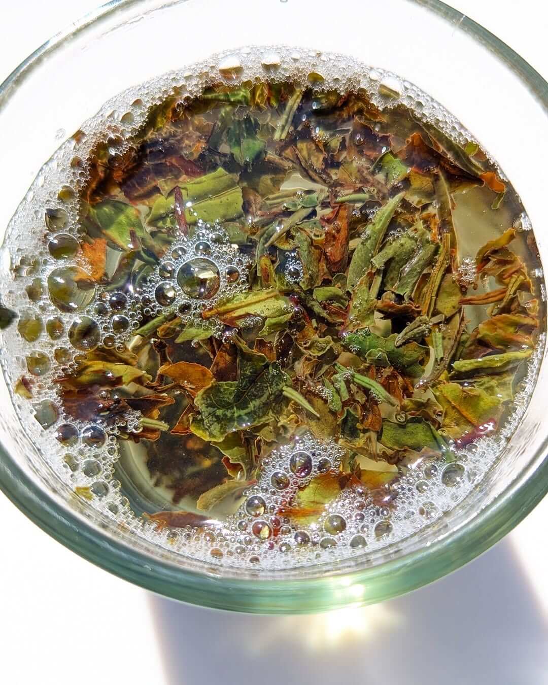 Brewed Aambari AV2 organic first flush black tea in a glass, showcasing loose leaves and bubbles.