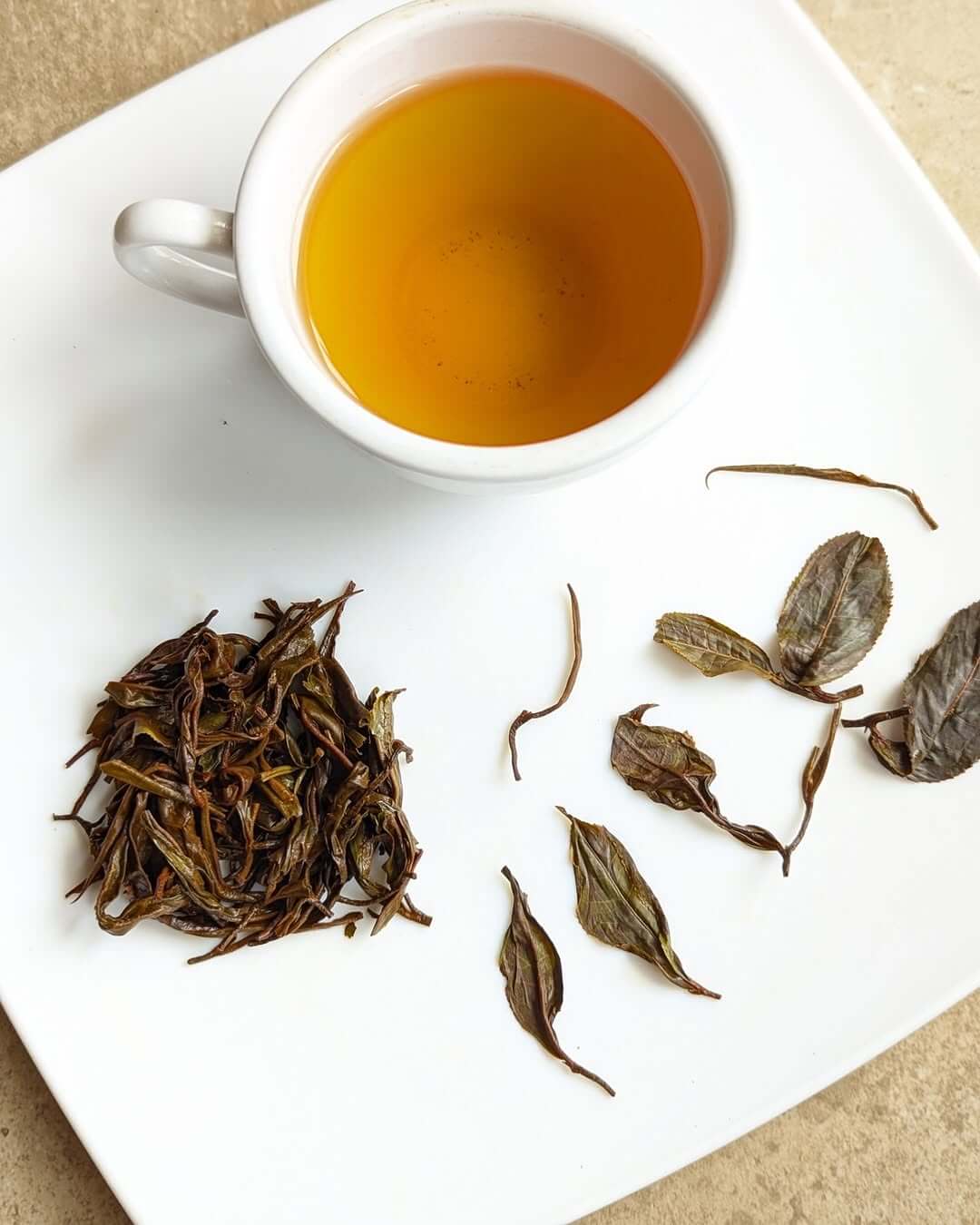 Cup of organic black tea with loose leaves on a white plate, showcasing premium quality herbal infusion.