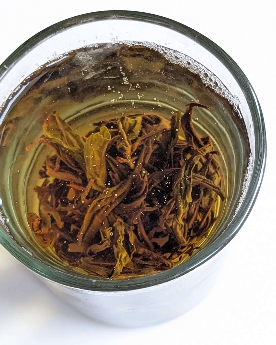 Glass cup filled with brewed P-126 Clonal Tippy Reserve Organic Black Tea, showcasing loose leaf tea and golden color.